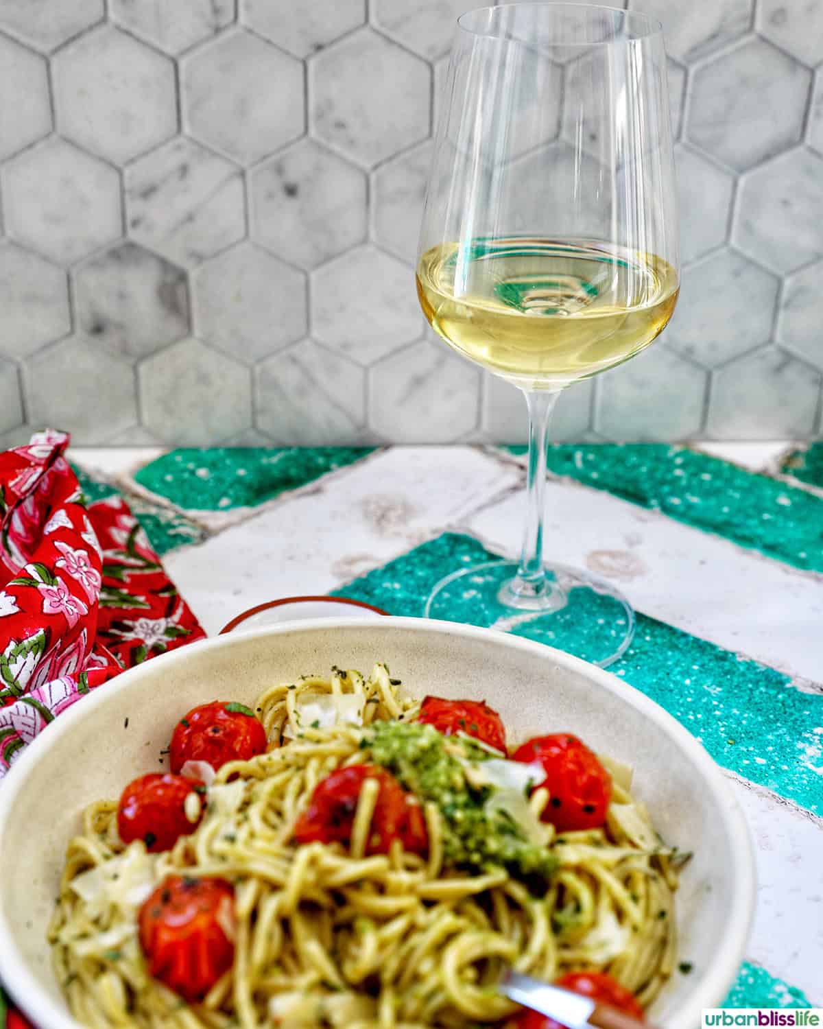 bowl of cherry tomato and pesto pasta with a glass of white wine.