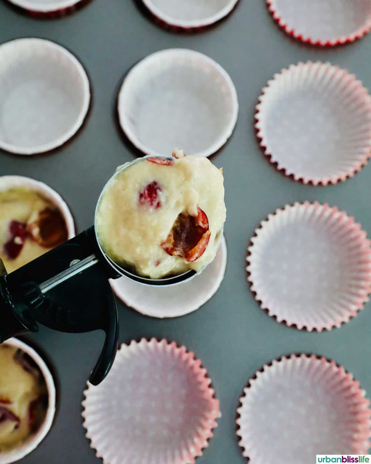 scoop of cherry muffin batter over empty cupcake liners in a tin.