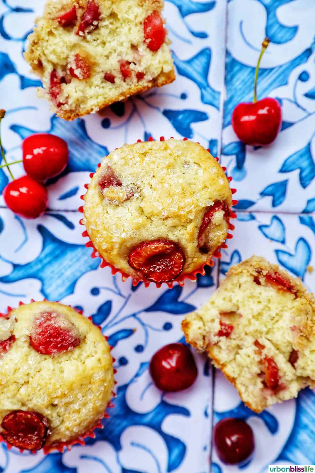 stack of cherry muffins with fresh cherries on a blue and white table.