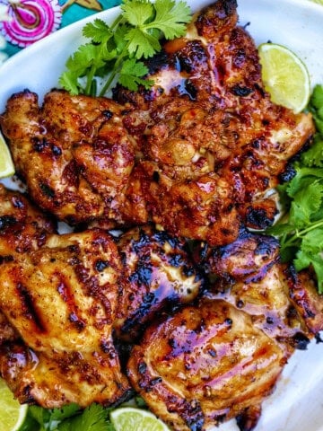 Filipino grilled chicken inasal on a platter with lime wedges and cilantro.