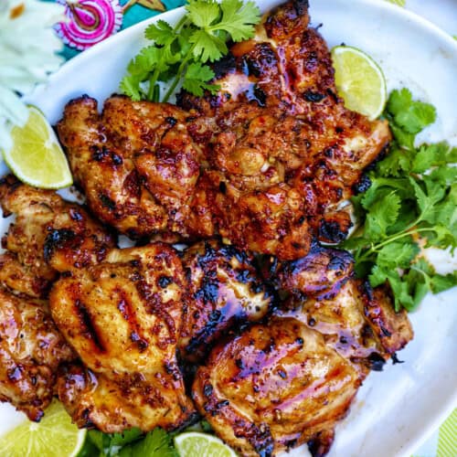 Filipino grilled chicken inasal on a platter with lime wedges and cilantro.
