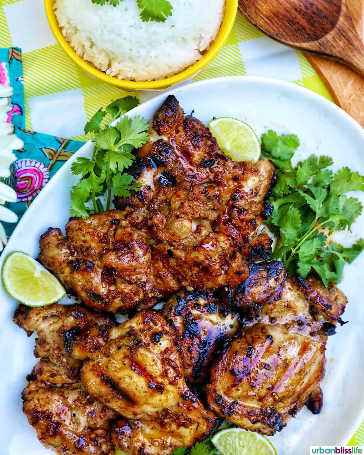 Filipino grilled chicken inasal on a platter near a bowl of rice.