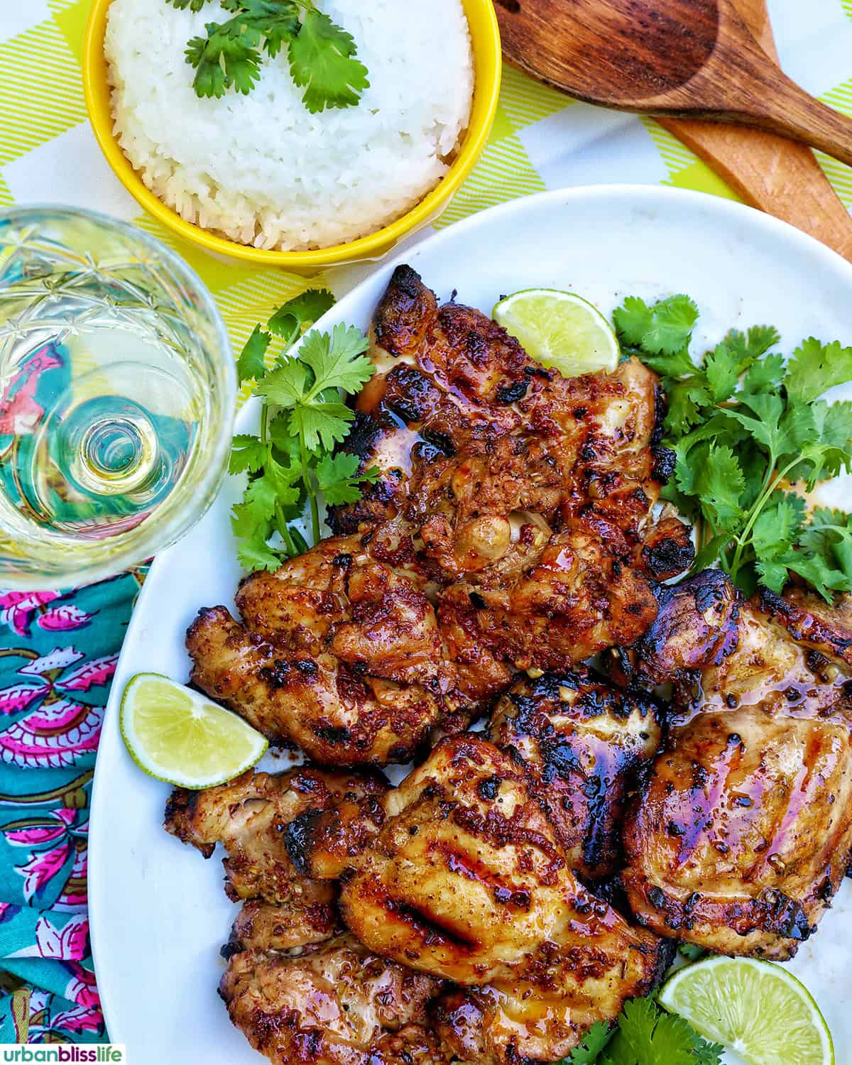 Filipino grilled chicken inasal on a platter near a glass of white wine and bowl of rice.