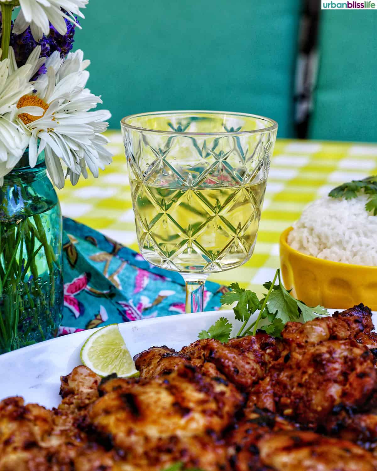 Filipino grilled chicken inasal on a platter near a glass of white wine and bowl of rice.
