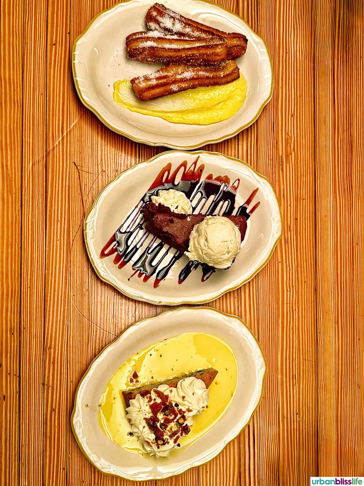 three desserts on plates on a wood table.