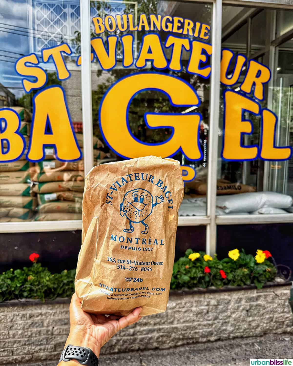 outside of St Viateur bagels with hand holding a bag of bagels.